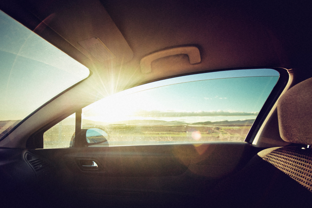A parked car sitting in direct summer sunlight with the dashboard and steering wheel visibly lit by bright sun, realistic photo