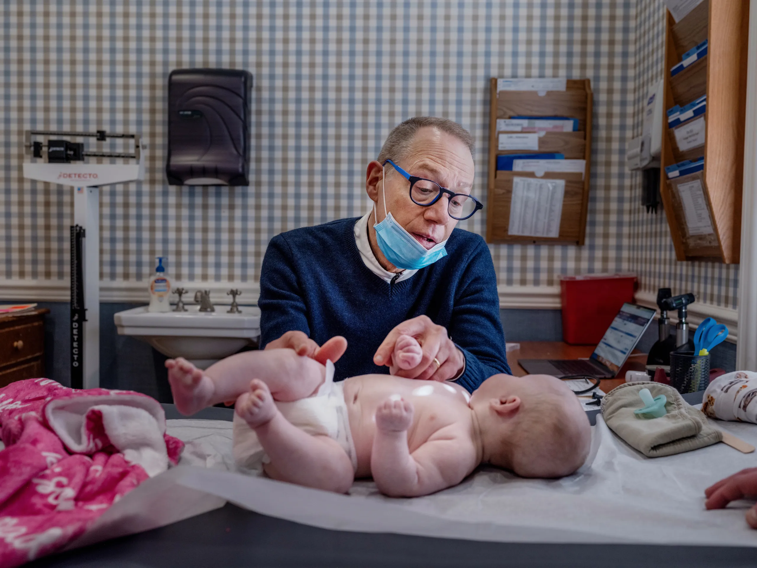 A pediatric clinic nurse gently examining a child’s wrist with scattered small red spots, realistic clinical photo