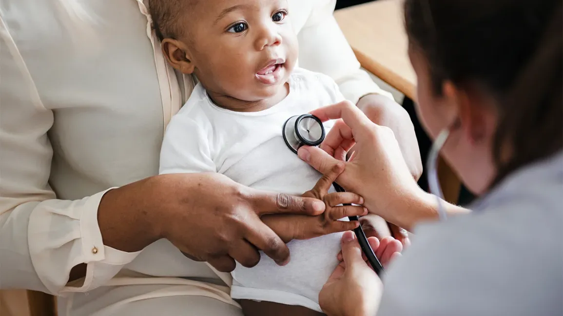 A pediatric clinician gently listening to a toddler's lungs with a stethoscope in a clinic exam room while a parent sits nearby, warm natural light, photorealistic