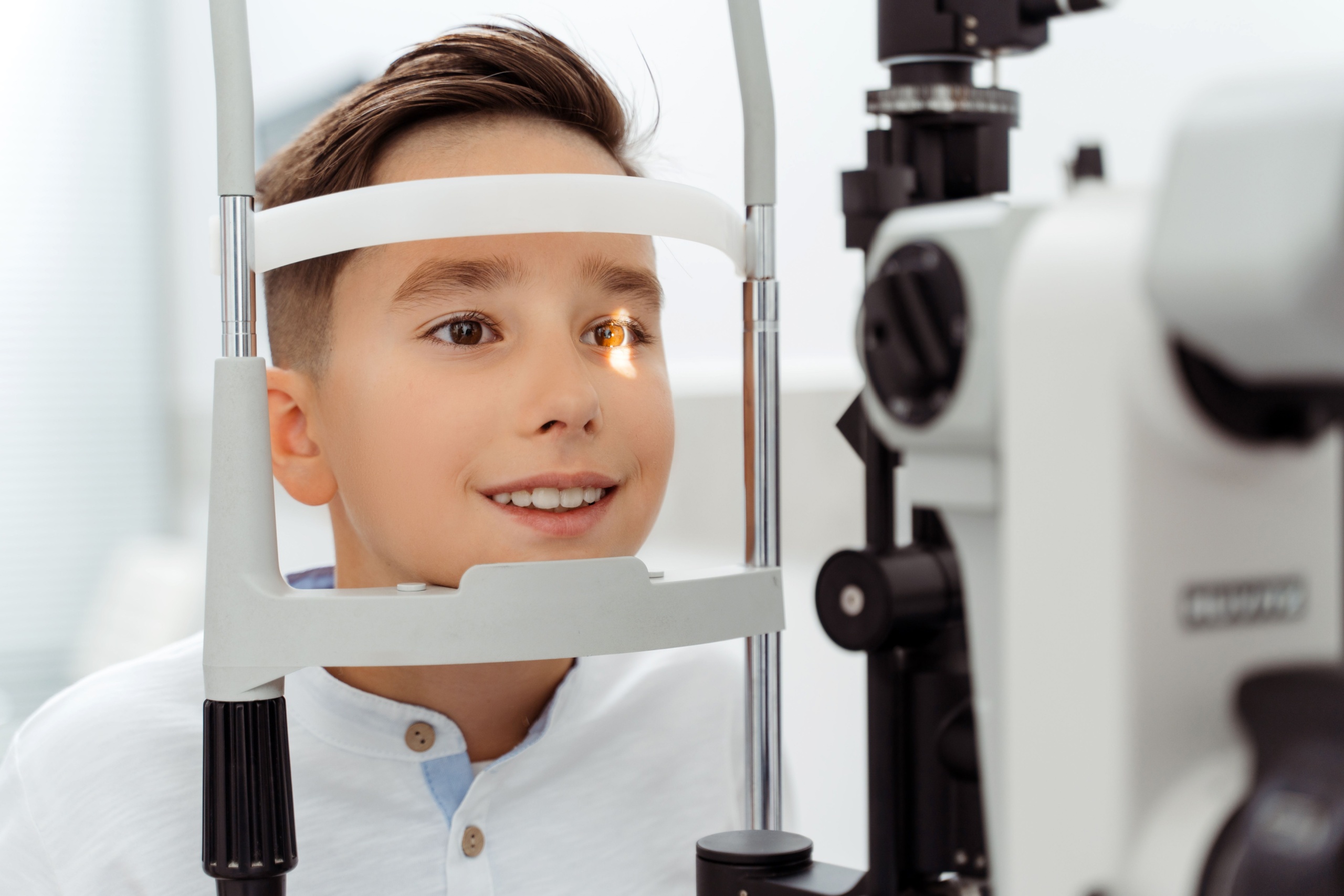 A pediatric ophthalmologist performing a slit-lamp eye exam on a young child while a parent sits nearby