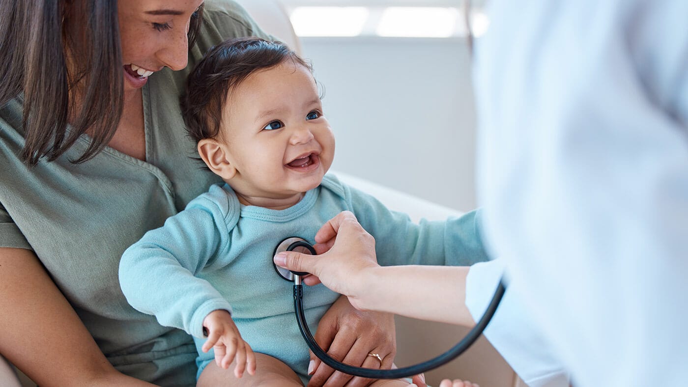 A pediatrician listening to a baby’s lungs with a stethoscope in a clinic exam room while a parent holds the baby, realistic clinical photo