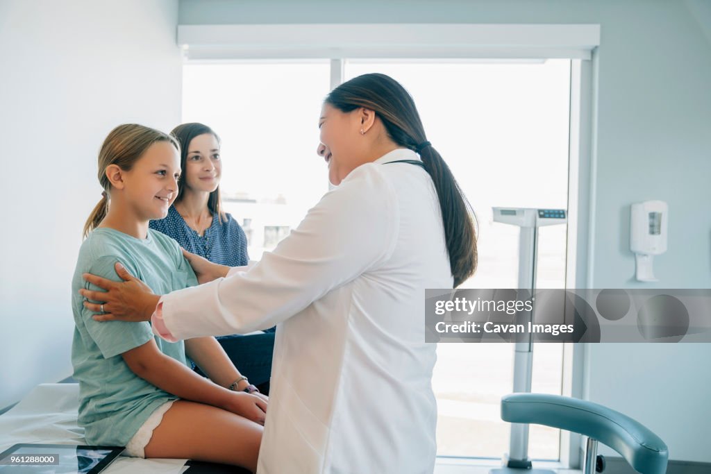 A pediatrician seated in a clinic exam room speaking with a parent who is holding a toddler, calm reassuring medical visit photo
