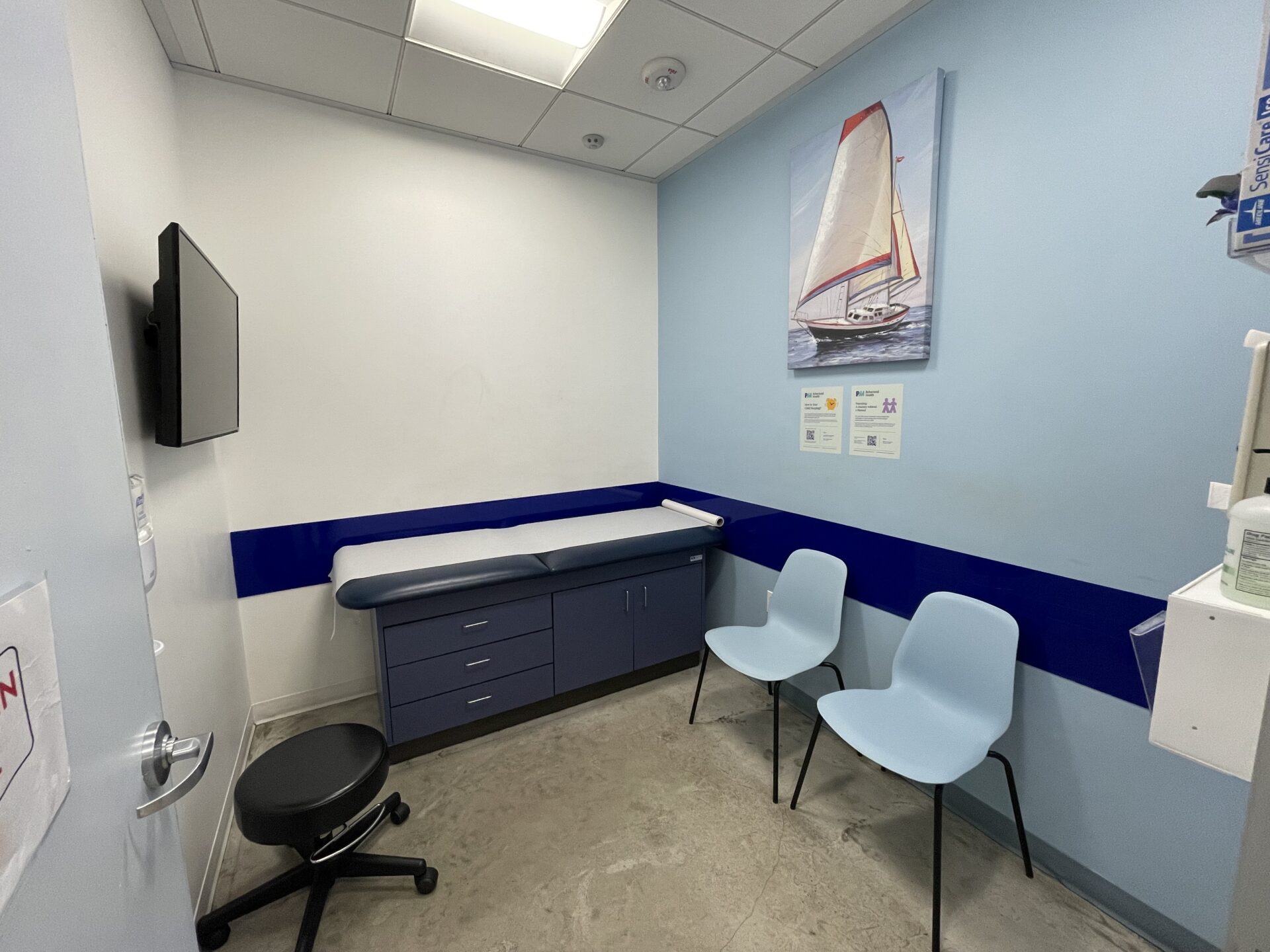A photo of a pediatric urgent care exam room with a clinician’s gloved hands applying a small gauze dressing to a child’s upper arm