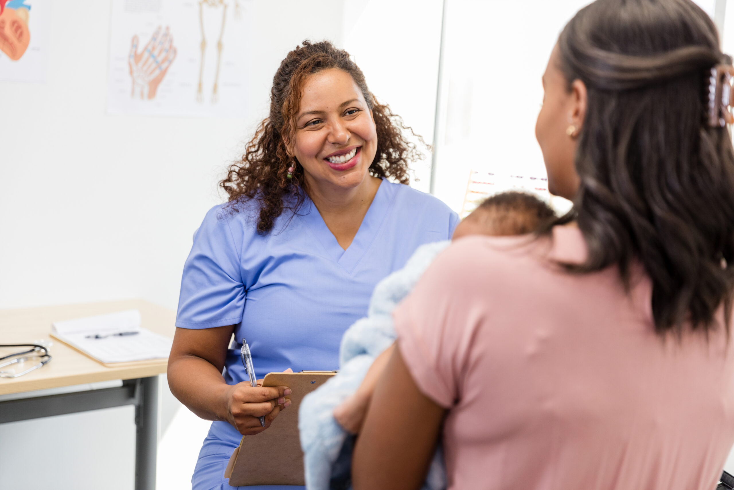A postpartum parent sitting in a medical exam room speaking with a clinician in a calm, supportive conversation, realistic photography