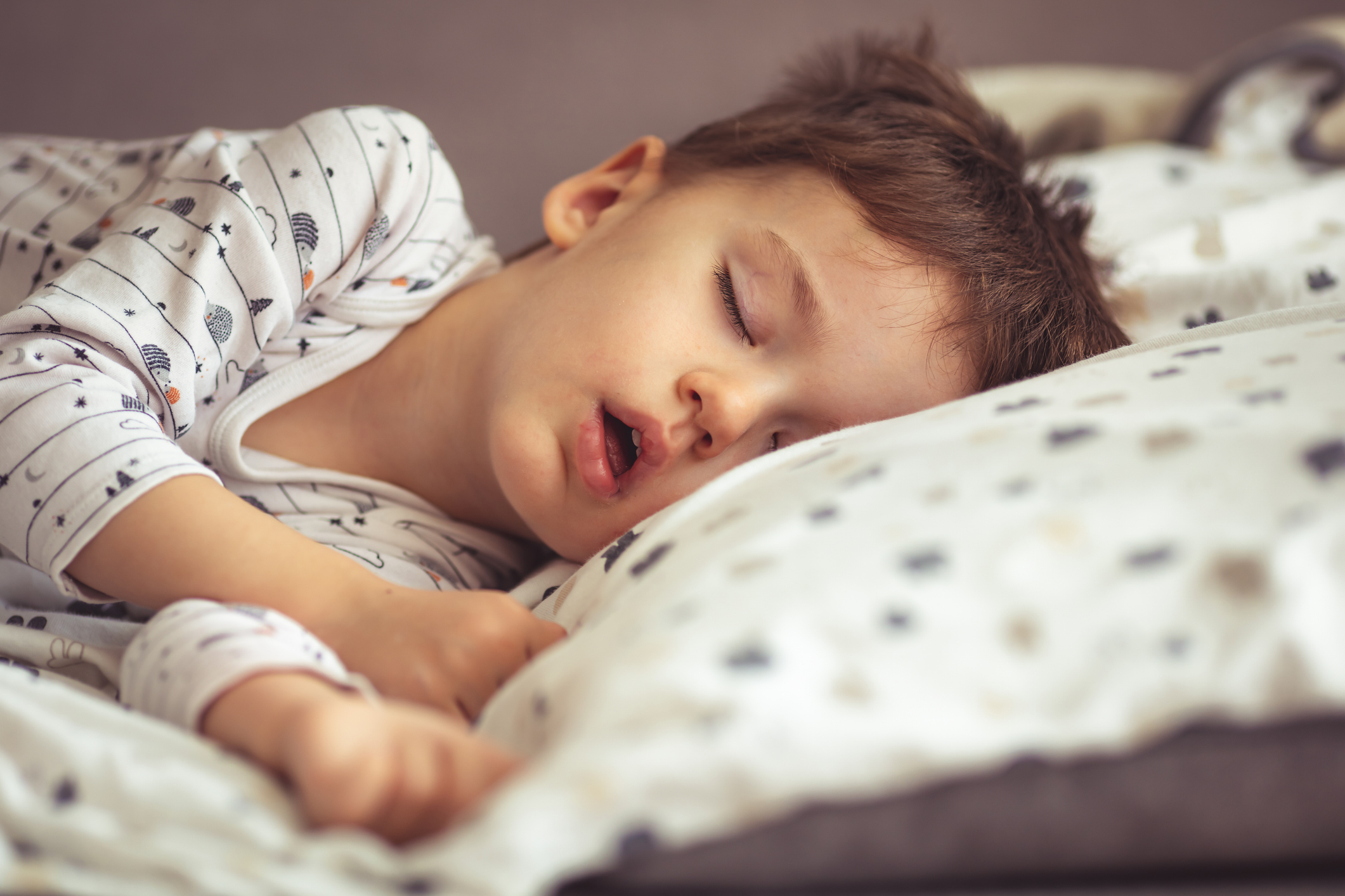 A preschool-aged child asleep with their mouth slightly open, head turned to the side on a pillow, low light bedroom setting, realistic candid photography
