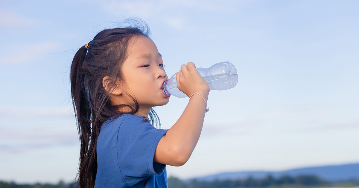 A preschool-aged child sitting up in bed at night taking a sip of water while a parent sits nearby, soft bedside lamp lighting