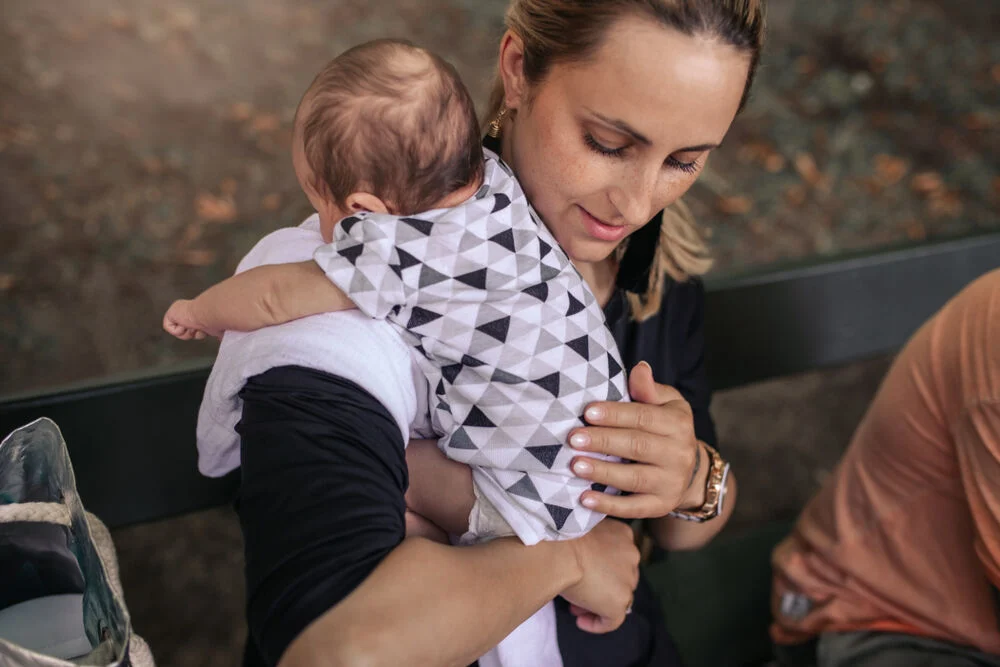 A real-life photo of a parent burping a newborn baby over their shoulder with the baby supported at the chest and head, a burp cloth on the parent’s shoulder, warm indoor lighting