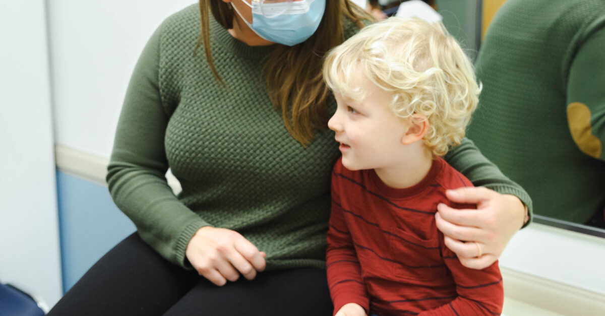 A real-life photo of a tired toddler resting on a parent’s shoulder in a clinic waiting room with soft indoor lighting