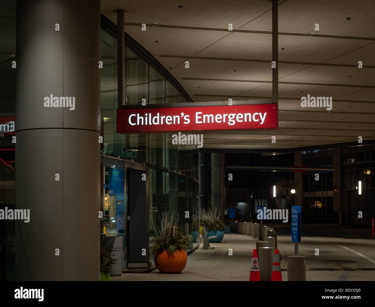 A real photo of a hospital emergency department entrance at night with lights on and a parent carrying a small child toward the doors