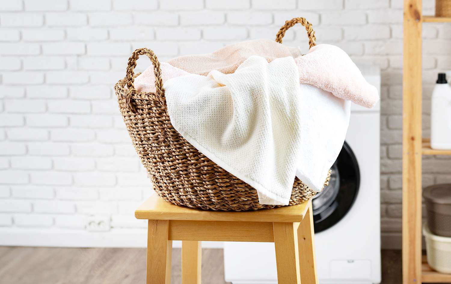 A real photo of a laundry basket filled with white bedding next to a washing machine, suggesting hot washing and drying as part of home cleaning