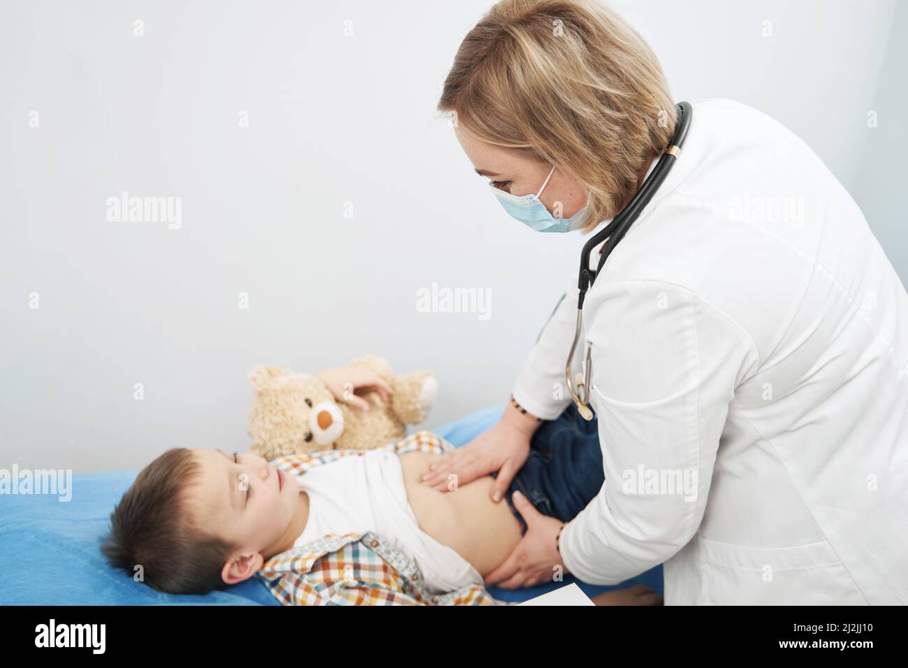 A real photo of a pediatrician gently examining a baby's abdomen during a routine checkup in a bright clinic room