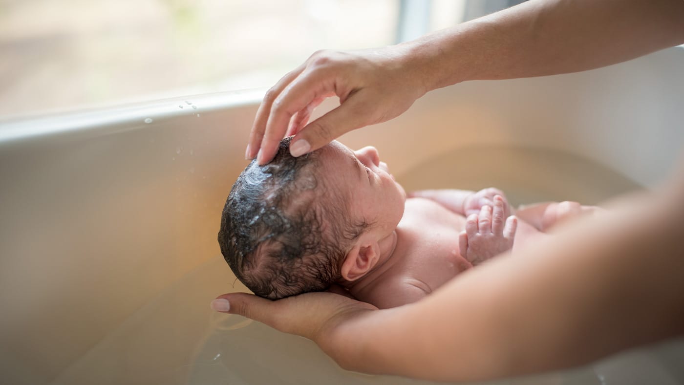 A real photo of a relaxed baby wrapped in a soft towel after a bath, with clean cheeks and chin in warm indoor light