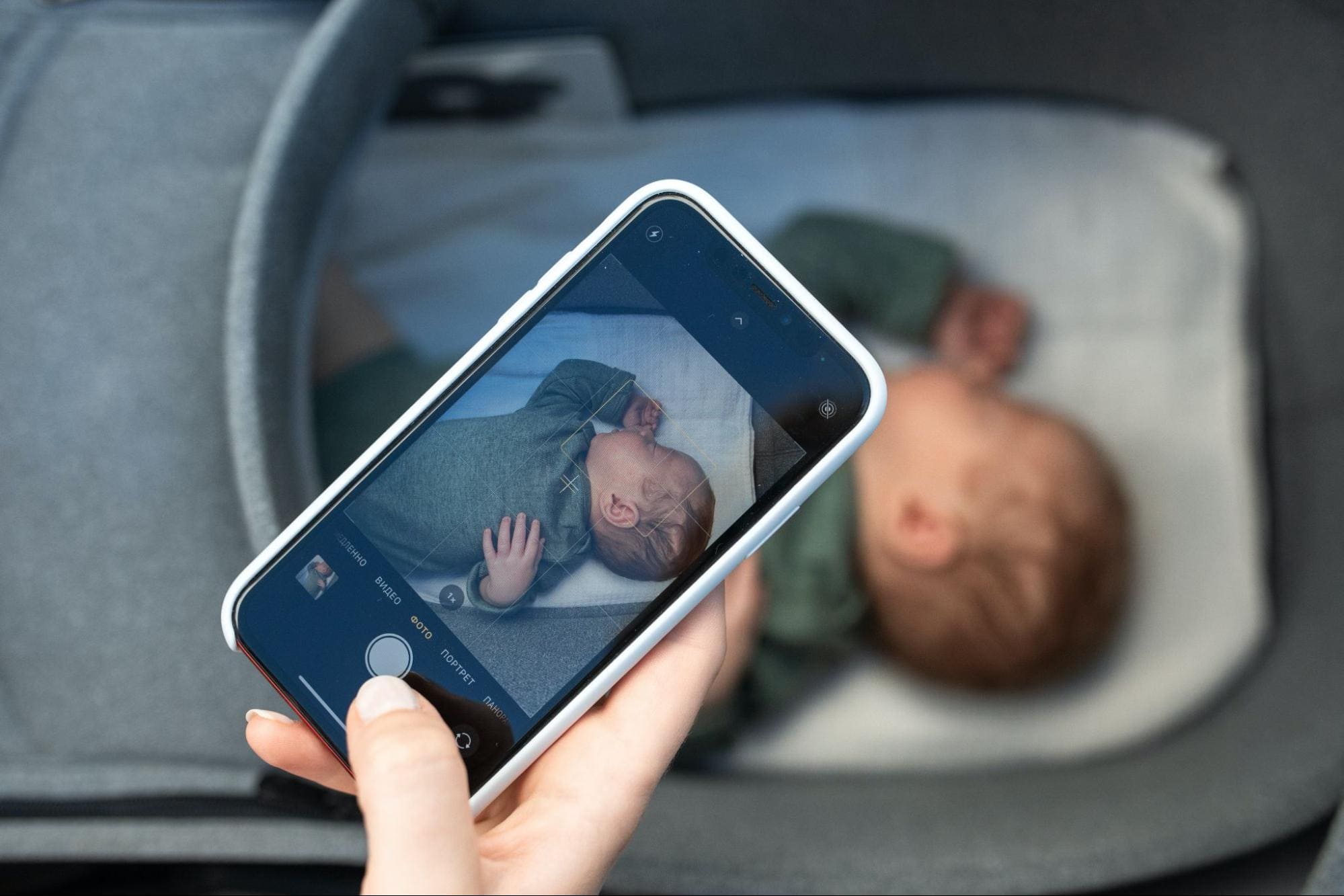 A real photograph of a parent holding a smartphone and taking a close-up photo of a baby’s arm to track a small red birthmark, warm indoor lighting