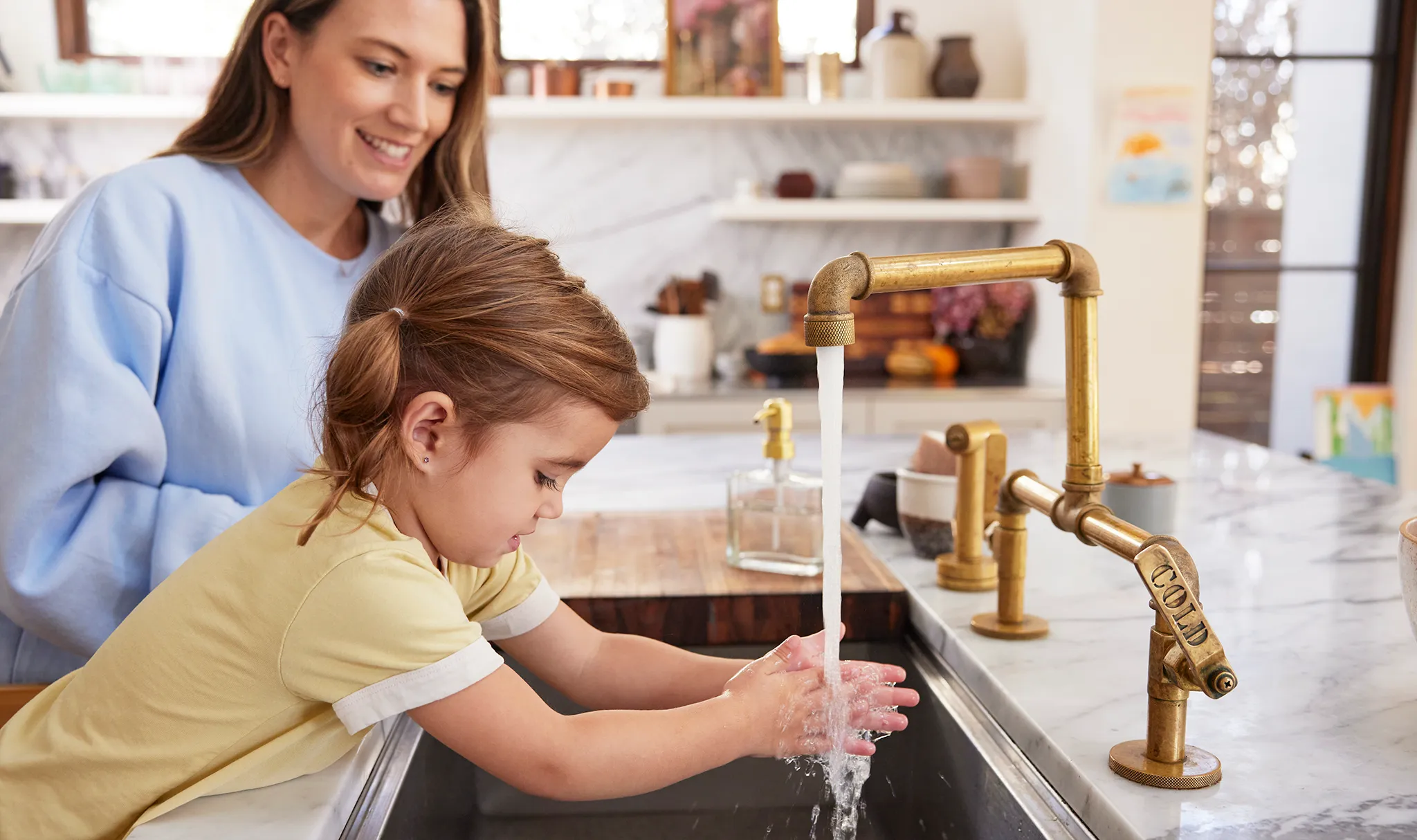 A real photograph of a parent washing a young child’s hands with soap at a bathroom sink, focusing on thorough rinsing under running water