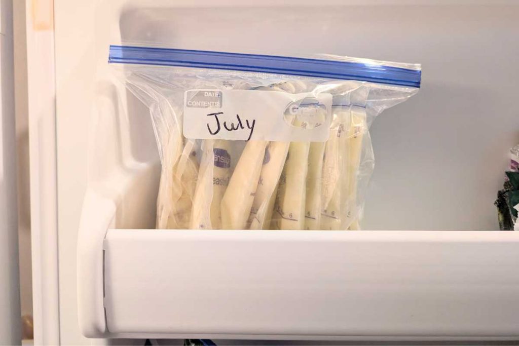 A realistic photo of a freezer drawer containing neatly stacked breast milk storage bags with handwritten dates, no visible brand logos, soft indoor lighting
