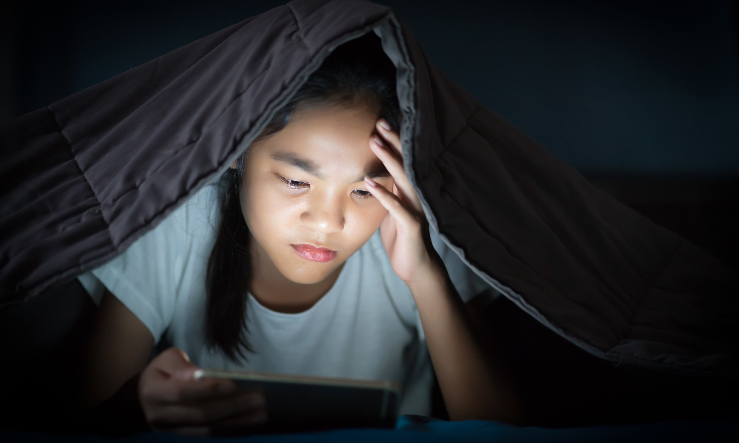 A school-age child resting on a couch in a dim, quiet living room with a cool washcloth on their forehead while a parent sits nearby, real-life photography style