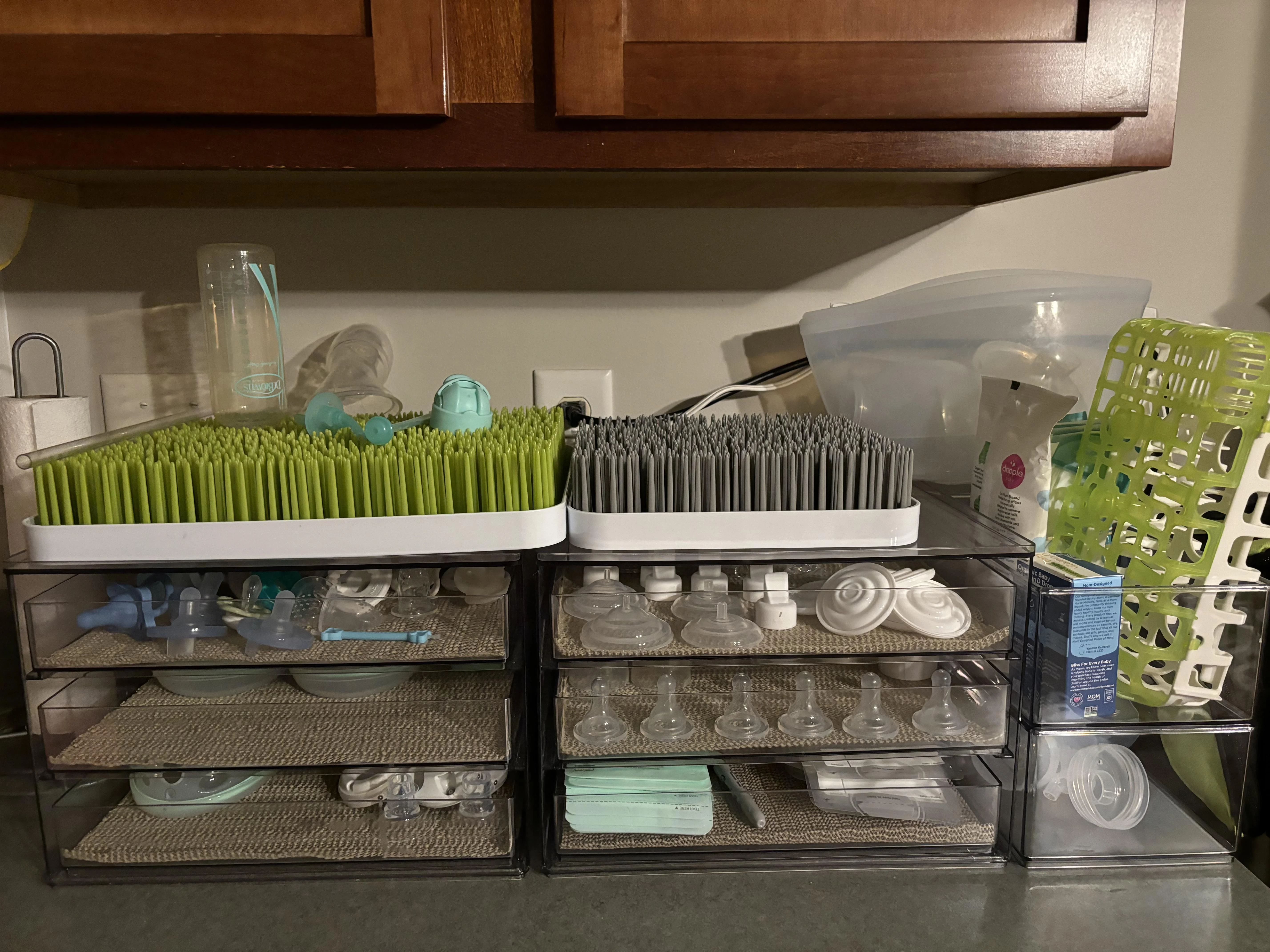 A tired but calm parent sitting at a kitchen table in soft morning light using a double electric breast pump, with clean pump parts and a water bottle nearby, realistic photo