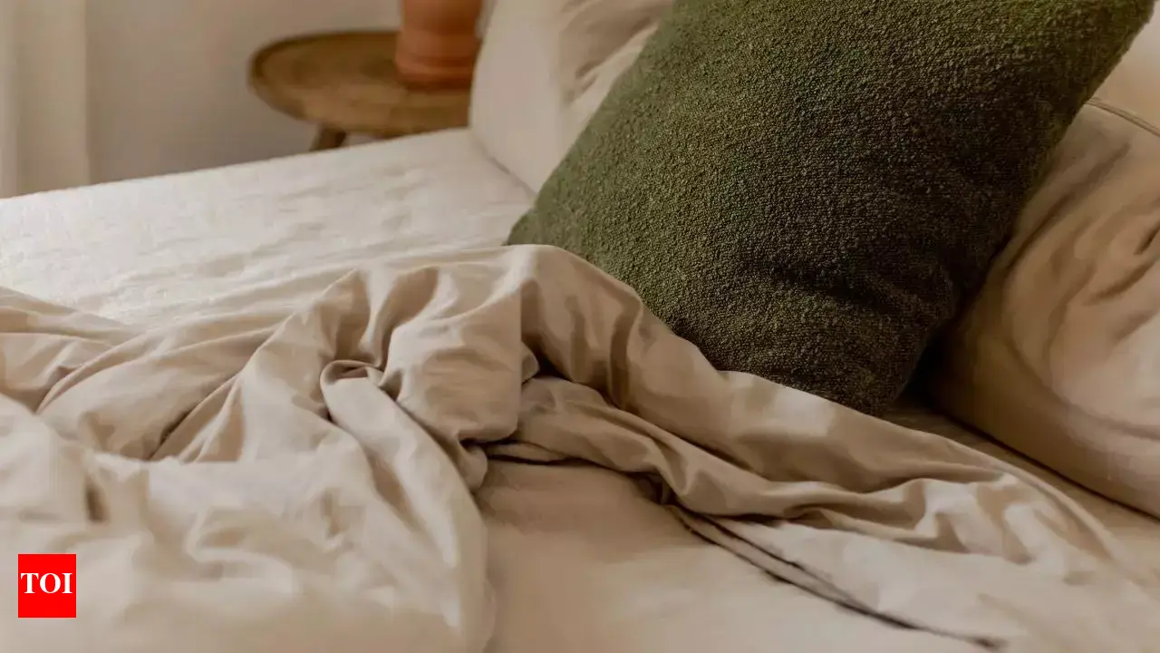 A tired parent changing a child’s bed sheets in a dimly lit bedroom at night, with clean pajamas folded nearby