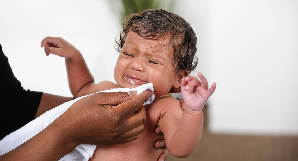 A tired parent gently holding a baby near a kitchen high chair after a vomiting episode, realistic indoor family photograph
