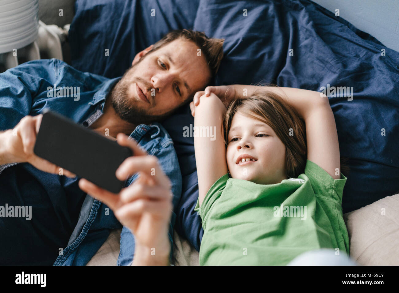 A tired parent sitting on a couch at night looking closely at a smartphone photo of their toddler, warm indoor lighting, candid lifestyle photograph