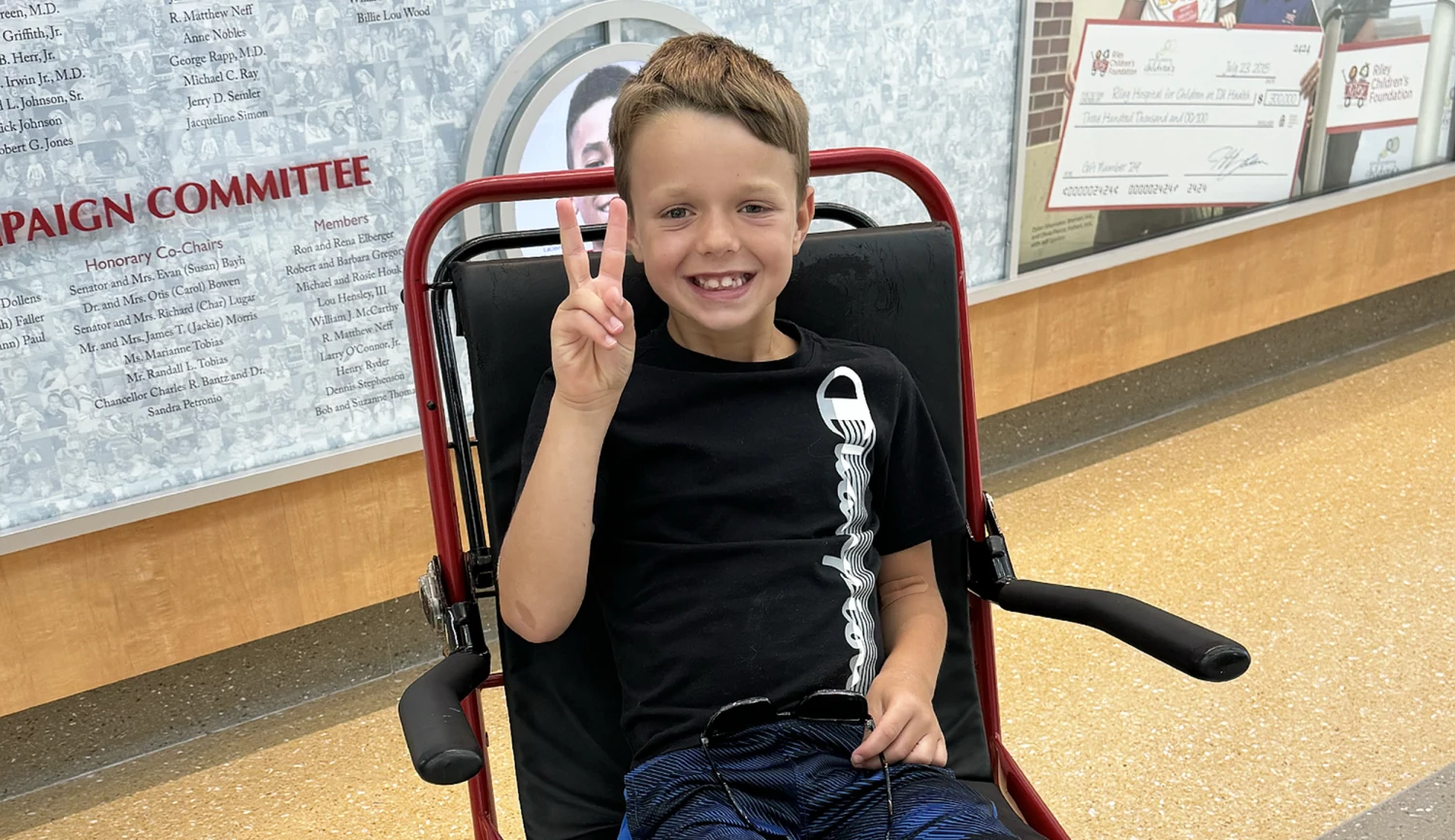 A tired toddler in pajamas sitting on a living room floor, clutching their belly and drawing knees up with a distressed expression, natural home lighting, real-life photo