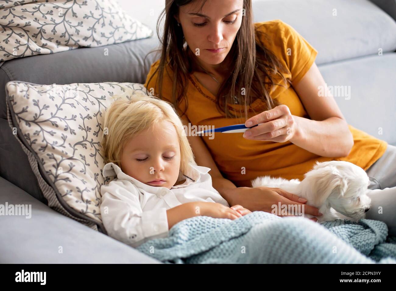A tired toddler resting on a parent's shoulder on a living room couch with a blanket, natural window light, realistic photo