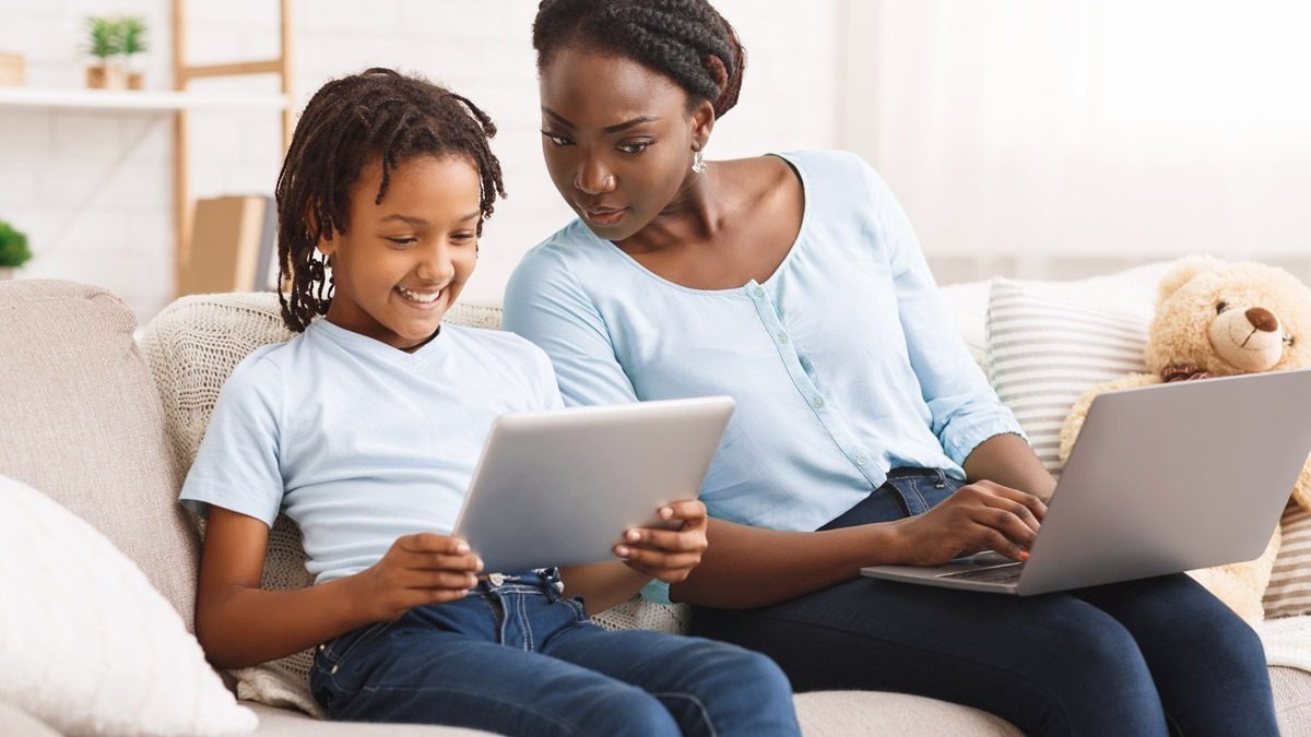 A tired toddler resting their head on a parent’s shoulder on a couch in a softly lit living room, realistic photo
