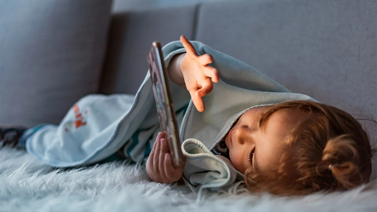A toddler asleep on a small bed in a quiet living room with soft daylight coming through a window, realistic home photograph