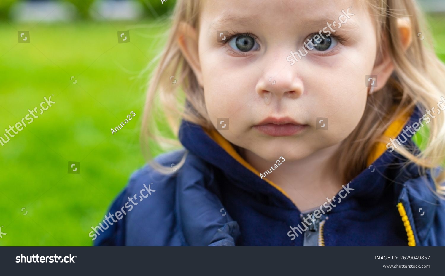 A toddler in a grassy park with a clear runny nose and slightly watery eyes, wearing a light jacket during springtime, real photo style