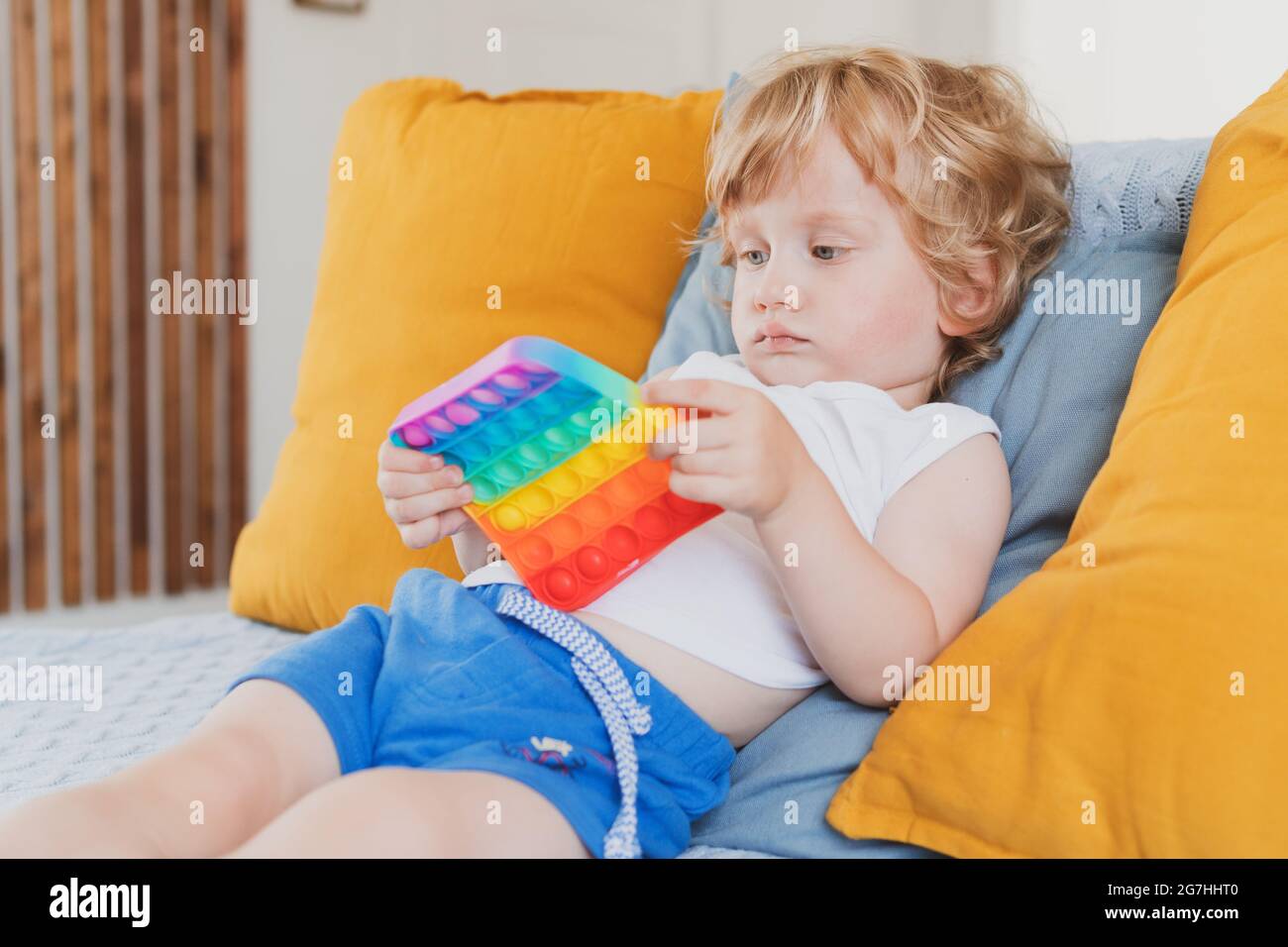 A toddler sitting in a car seat holding a small textured sensory fidget toy in their hands, natural daylight through the window, realistic photograph