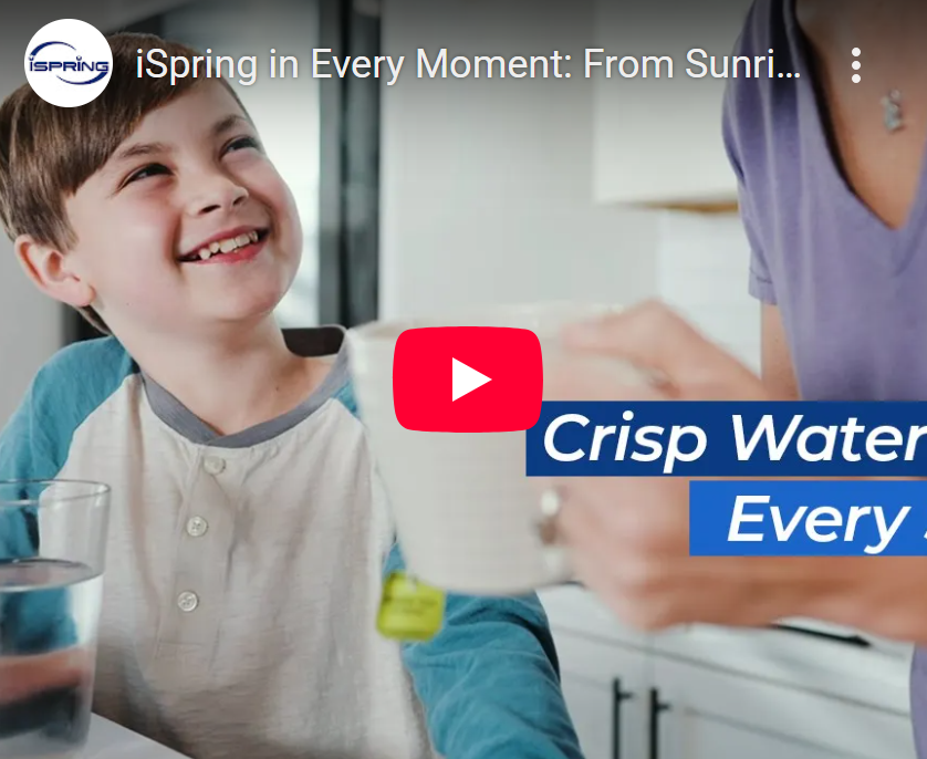 A toddler sitting in a kitchen high chair taking a sip from a small water cup while a parent watches nearby, realistic family photo