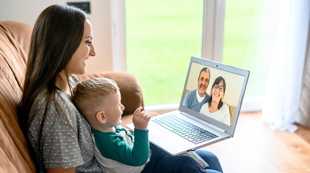 A toddler sitting on a couch holding a tablet during a video call with a smiling grandparent, cozy living room photography style