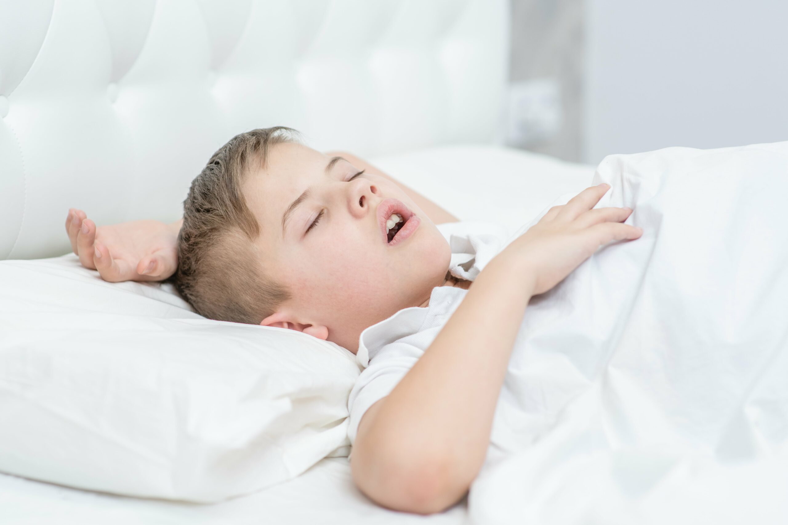 A toddler sleeping in a dim bedroom with their mouth slightly open and soft night light in the background, natural lifestyle photograph