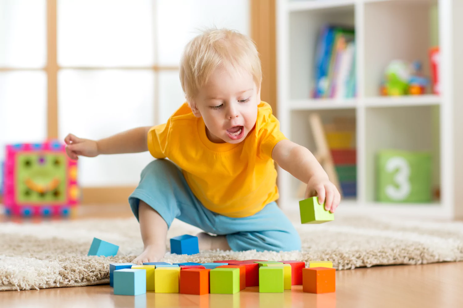A toddler stacking wooden blocks on a kitchen floor while a parent sits nearby watching attentively, natural candid photo