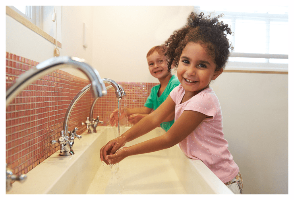 A toddler standing on a step stool washing hands with soap at a bathroom sink, realistic home photo