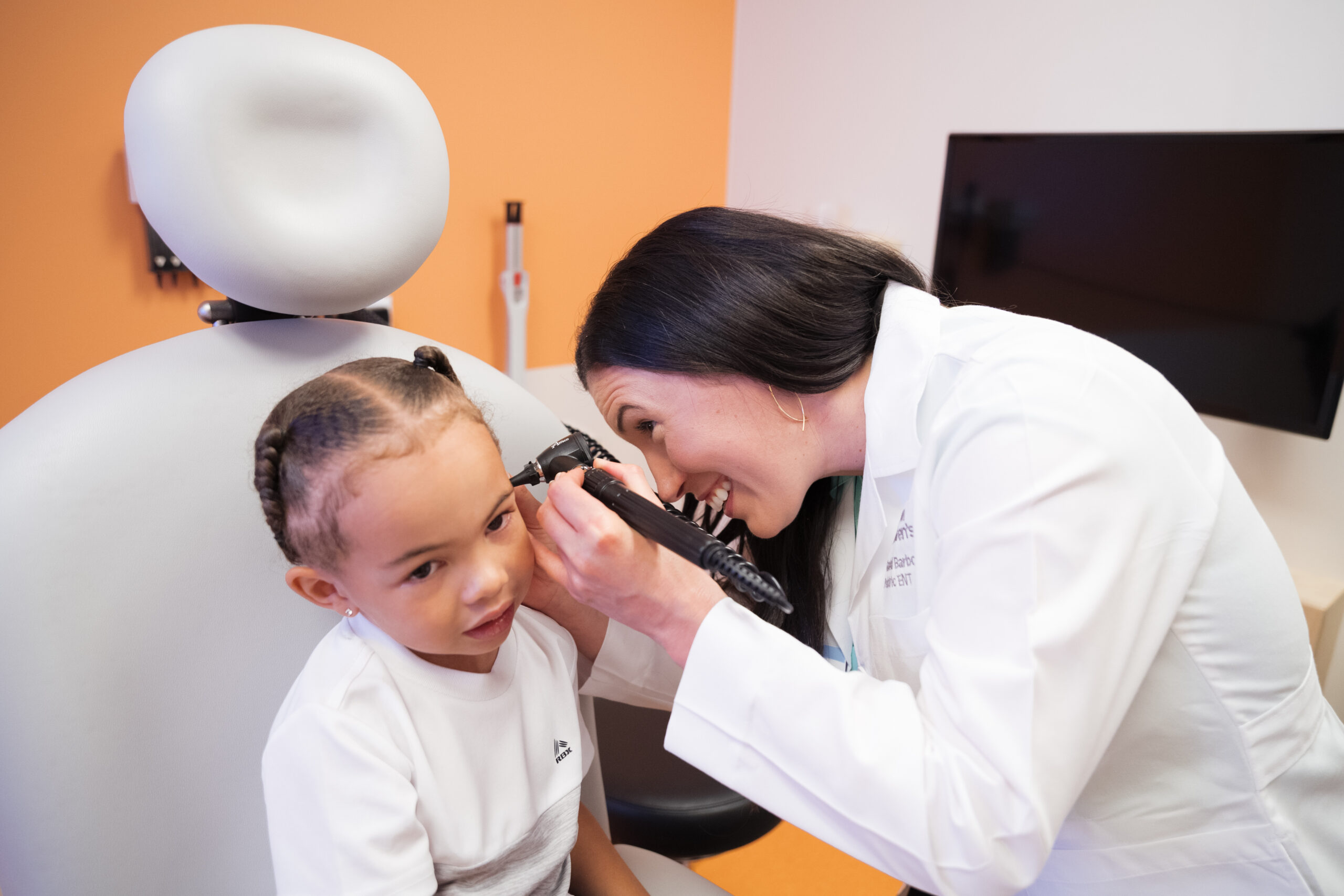 A young child sitting calmly during a basic hearing screening in a pediatric clinic room while a clinician prepares equipment