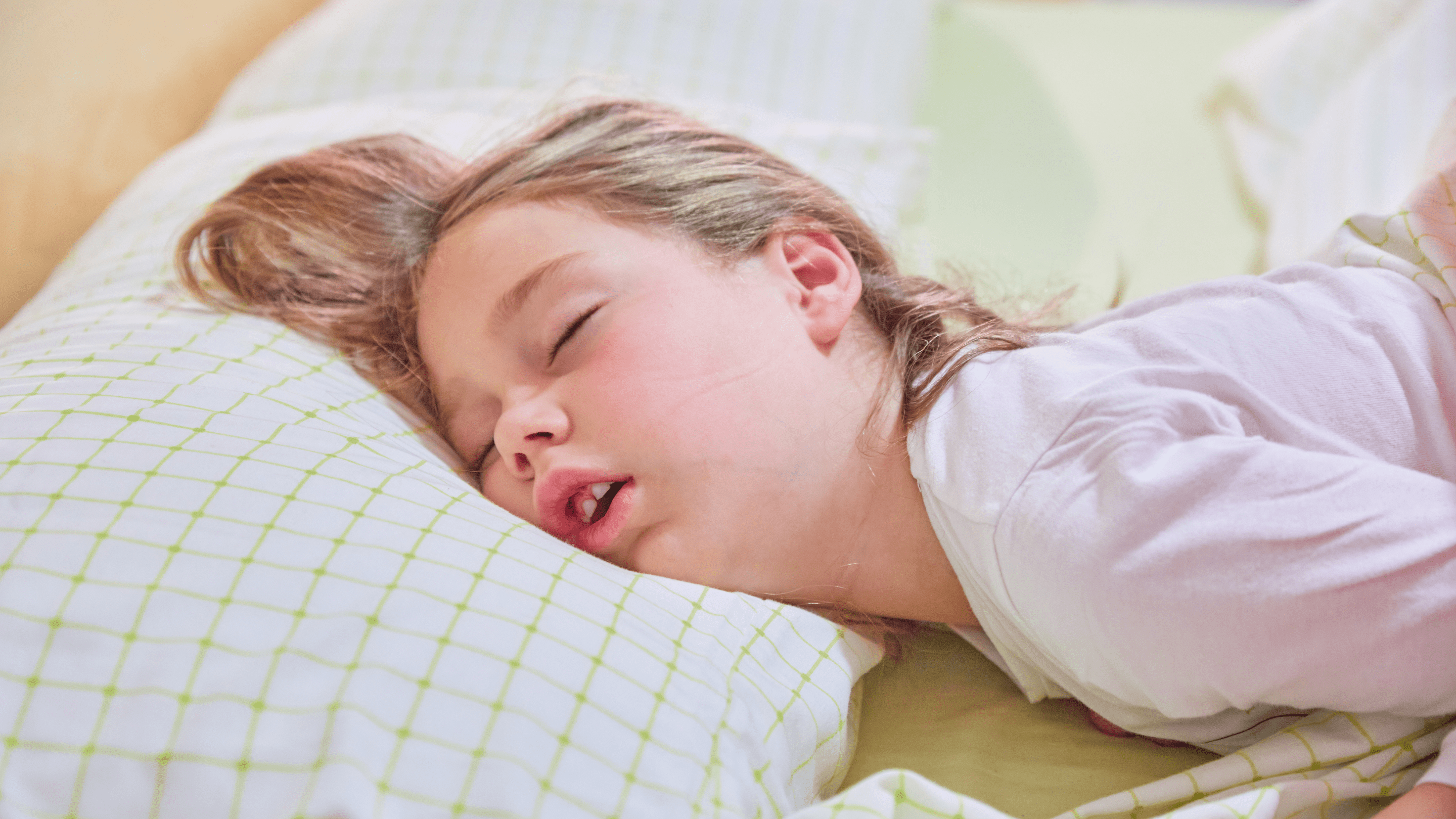 A young child sleeping on their side with their mouth slightly open on a pillow, nighttime bedroom lighting, realistic photo