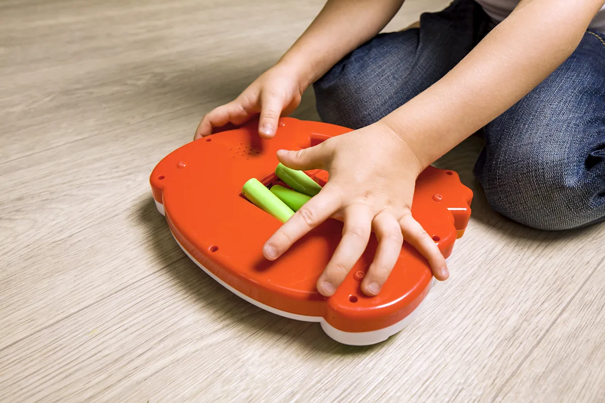 Close-up of an adult's hands using a small screwdriver to secure a toy battery compartment door on a child's toy, realistic home photo